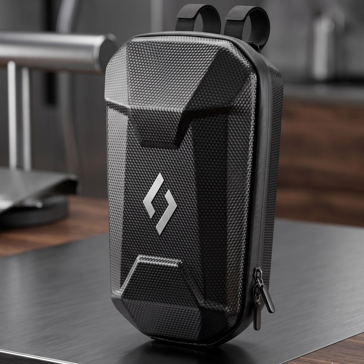 A black textured zippered utility bag with a silver geometric logo, standing on a dark tabletop in a modern indoor setting.